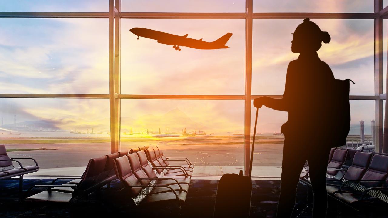 Person in airport looking at plane flying