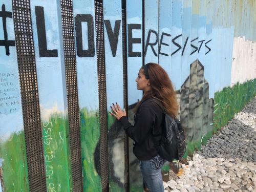 tania mendoza standing at border fence, looking through