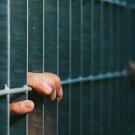 Hand of detained immigrant grasping at the prison cell door
